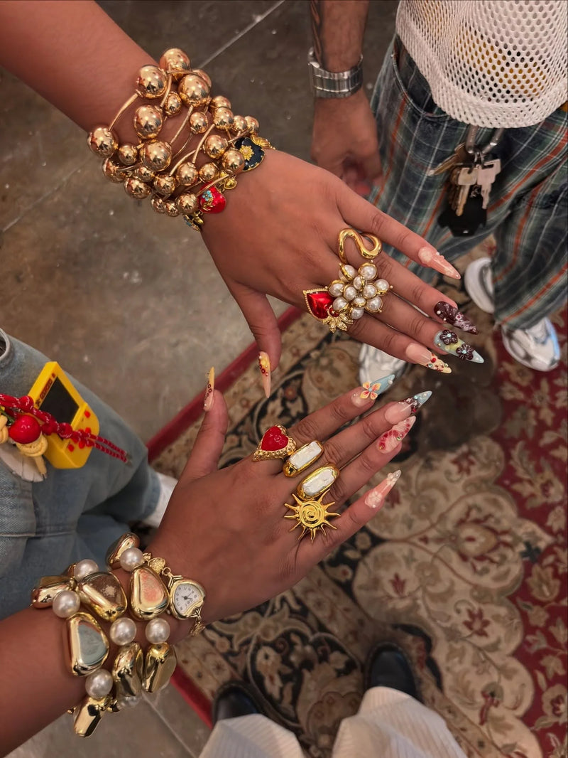 Close-up of hands wearing gold jewelry with intricate designs on a patterned rug.